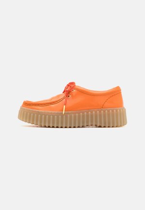 Orangefarbene Lederbootsschuhe mit einer runden Spitze, versehen mit roten Schnürsenkeln, besitzen eine dicke, geriffelte, durchsichtige beige Gummisohle.