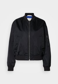 Černá bomber bunda vyrobená z hladkého, lesklého materiálu. Má přední zip, žebrované manžety a lem, a zipovou kapsu na rukávu.