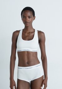 Weißer Baumwoll-Sport-BH und passende Unterhose mit tailliertem Design. Mit Calvin Klein-Logo auf einem kontrastierenden Bund. Glatte Textur.