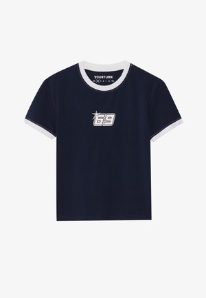 Navy blue puuvillapaita, jossa on valkoinen ribbireuna kauluksessa ja hihansuissa. Etupuolella on graafinen kuvitus, jossa on "69" ja tähden muoto. Lyhyet hihat, rento malli.