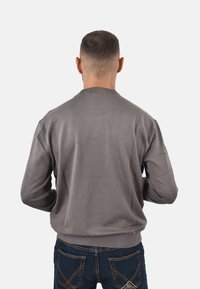 Suéter gris de punto, con cuello redondo y puños acanalados, combinado con jeans de mezclilla azul oscuro con detalles de costura visibles.