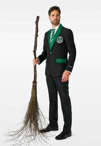 Schwarzer Anzug mit grünen Akzenten, versehen mit einem Wappen, kombiniert mit einer grün-weißen gestreiften Krawatte. Hält einen Besenstil aus Zweigen.
