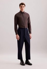 Bruin overhemd met knopen, donkerblauwe broek met brede pijpen, zwarte nette schoenen. Gladde stof, getailleerde pasvorm, klassieke kraag en zichtbare knopen.