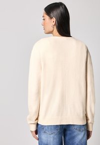 Pullover in maglia color crema con una vestibilità rilassata, scollatura rotonda e polsini e orlo ribattuti. Il materiale sembra morbido con una consistenza liscia.