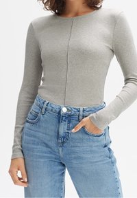 Long-sleeve, fitted top in light gray ribbed fabric with a seam down the center, paired with high-waisted, faded blue denim jeans.