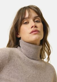 Hellbrauner Rollkragenpullover aus weichem, strukturiertem Stoff, mit einem gerippten Halsausschnitt und einer lockeren Passform. Entworfen für Wärme und Komfort.
