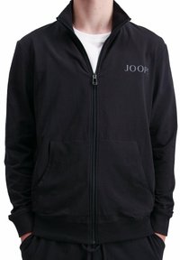 Schwarze Zip-Jacke aus weichem Stoff, mit hohem Kragen, zwei Fronttaschen und einem kleinen Logo auf der linken Brust.