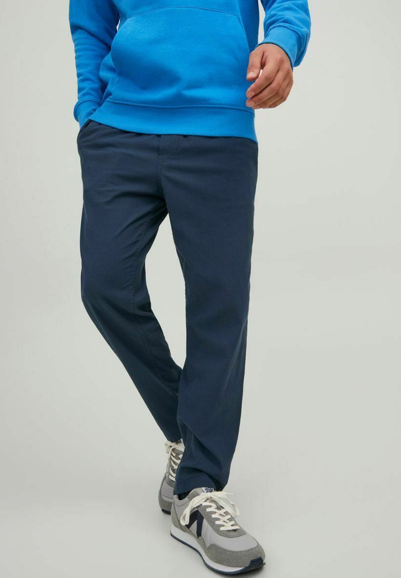 Marineblauwe broek in een relaxte pasvorm, gemaakt van gladde stof. Gecombineerd met grijs-witte sneakers met een mix van texturen en veters.
