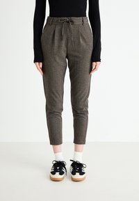 Pantaloni marroni con texture, vita con cordino, gambe affusolate e strisce laterali. Abbinati a sneakers nere e bianche e calzini alla caviglia.