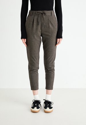 Bruine gemêleerde broeken met een elastische tailleband, taps toelopende pijpen en zijstrepen. Gecombineerd met zwart-witte sneakers en enkelsokken.