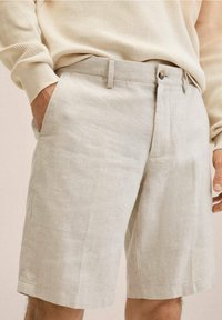Vaaleanbeiget pellavashortsit, joissa on suora leikkaus, etutaskut ja hillitty tekstuuri, täydentävät nappi- ja vetoketjukiinnitys.