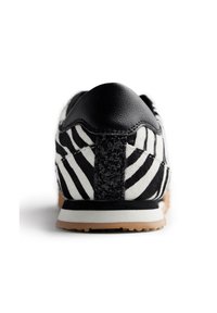 Sneaker a strisce zebrate in bianco e nero con tacco in pelle nera e dettagli in nero texturizzato. Suola in gomma con particolare in color sabbia.