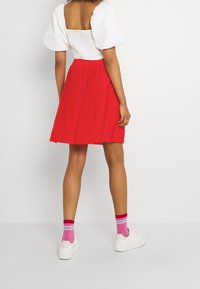 Červená plisovaná sukně doplněná bílým topem s balónovými rukávy. Bílé tenisky a růžové pruhované ponožky dokončují outfit. Hladká tkanina a přiléhavý střih.