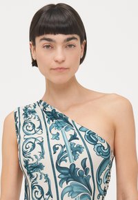 Asymmetrisk kjole i elfenben med teal blomster mønster. Glatt stoff med en tettsittende silhuett og rynkedetaljer på siden.