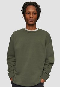 Grüner Baumwollpullover mit Rundhalsausschnitt, überschnittenen Schultern und gerippten Bündchen. Mit einem dezenten Logo auf der Brust.