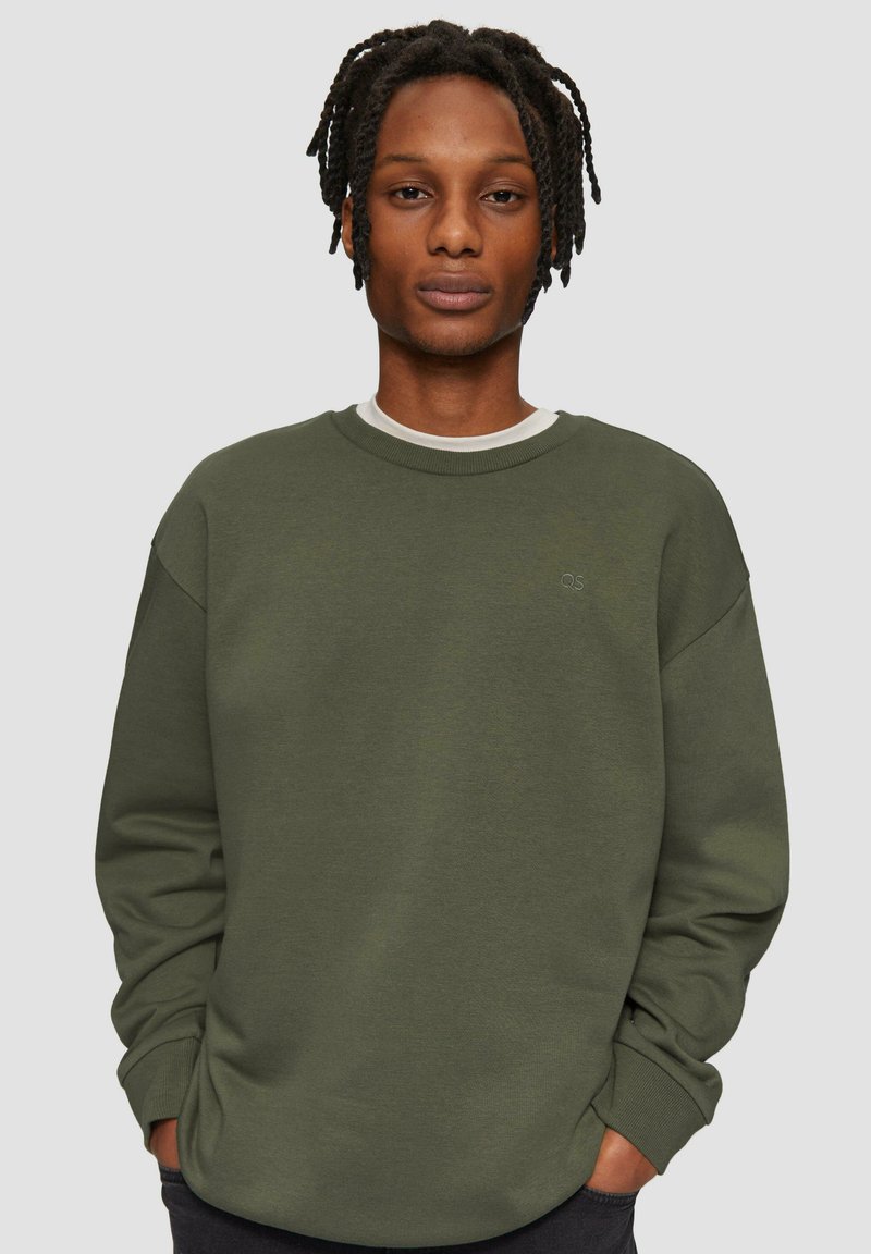 Grüner Baumwollpullover mit Rundhalsausschnitt, überschnittenen Schultern und gerippten Bündchen. Mit einem dezenten Logo auf der Brust.