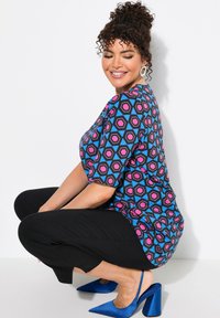 Top de patrón geométrico colorido en rosa, azul y negro, combinado con pantalones cortos negros y tacones de aguja azules.
