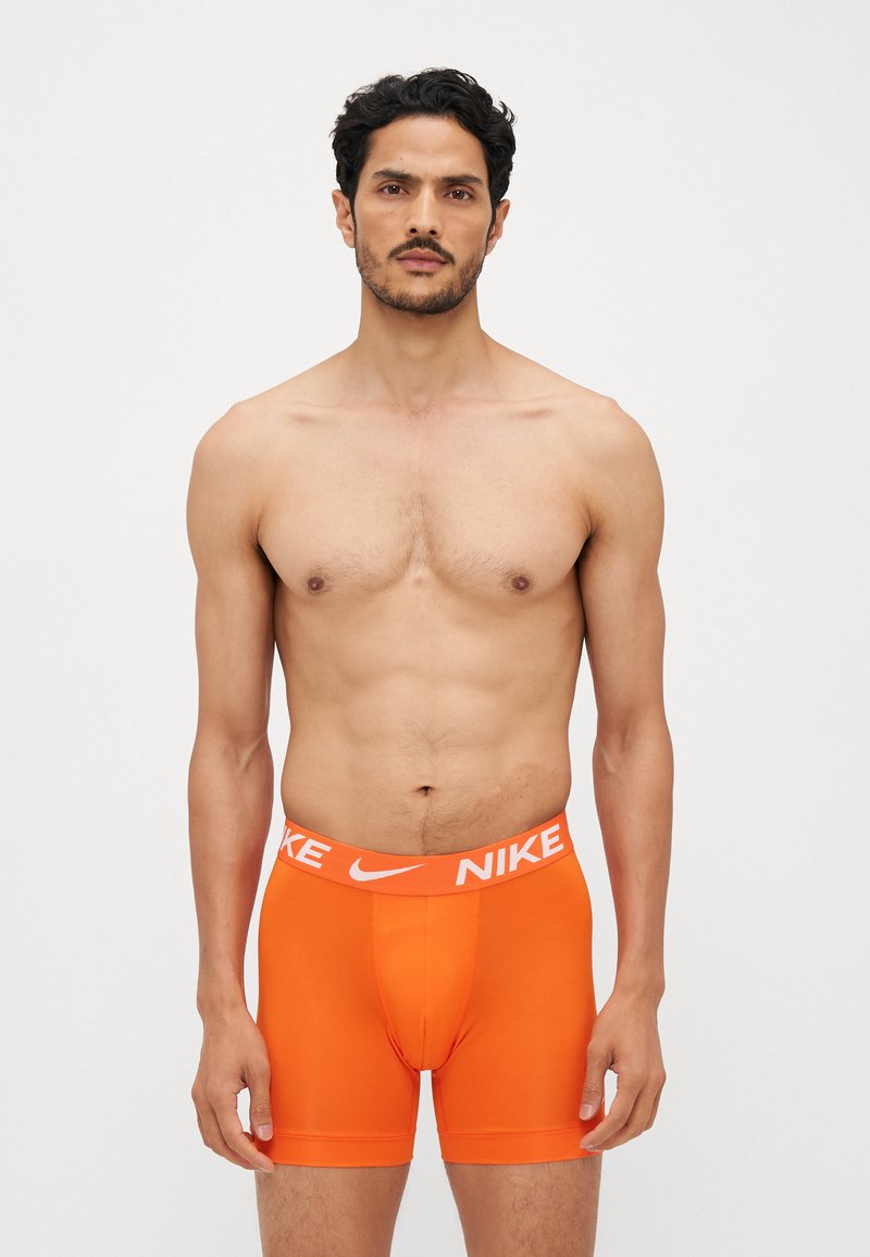 Orange moške bokserice iz razteznega materiala, z belim pasom z blagovno znamko in logotipom "Nike". Oblika, ki se prilega telesu.