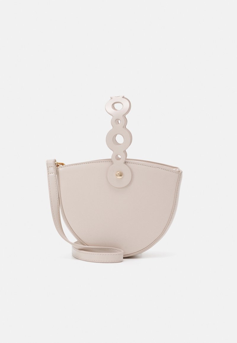 Beige half-moon bag made of smooth material, featuring a circular handle with cut-outs and a detachable shoulder strap. Gold hardware accents.