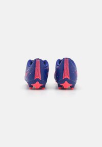 Fotballsko i lilla med rosa aksenter. Har en teksturert overflate og stjernesformede knotter for grep. Bakfra viser den en kontrastfylt design.
