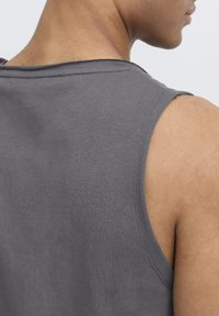 Graues ärmelloses Tanktop mit weicher Textur, runder Ausschnitt und unvollendeten Kanten an den Armausschnitten, von hinten betrachtet.