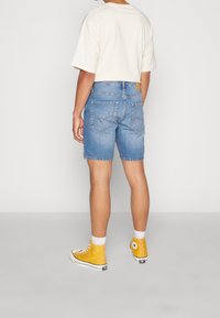 Shorts de mezclilla en azul claro, con un corte clásico, bolsillos traseros con detalles de costura, combinados con una camiseta oversized beige y zapatillas amarillas.