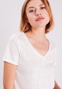 Weißes kurzärmliges T-Shirt mit V-Ausschnitt und dekorativen Nähten am Kragen. Weicher Stoff und lockere Passform.
