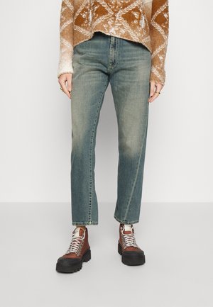 Jeans rectos de color azul claro con un acabado desgastado, combinados con botas de senderismo marrones con suelas negras y cordones plateados, y un suéter marrón de estampado.
