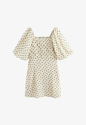 Robe crème à pois noirs, manches bouffantes jusqu'au coude, encolure carrée, et plis horizontaux sur la poitrine.