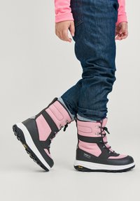 Botas impermeables en rosa y gris con parte superior de tela texturizada, ojales de metal y suela Vibram, combinadas con jeans de mezclilla.
