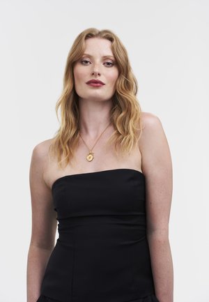Zwarte strapless top met een aansluitend ontwerp, een gladde textuur en subtiele details. Het model draagt een gouden hangersketting.