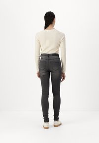 Grå skinny jeans med høy midje, kombinert med en kremfarget ribbet langermet topp. Fottøyet består av hvite joggesko med gummisåle.
