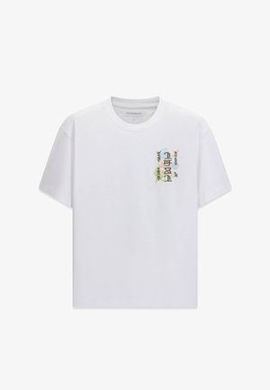 Weißes T-Shirt mit kurzen Ärmeln und kleinem, buntem, vertikal angeordnetem Motiv aus abstrakten Formen und stilisierten Figuren auf der linken Brust.