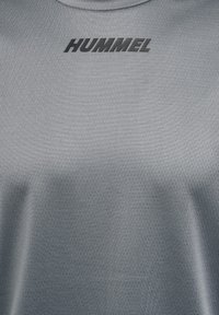 Tessuto grigio testurizzato con logo nero "HUMMEL" stampato vicino alla parte superiore centrale, simile a materiale per abbigliamento sportivo o atletico.