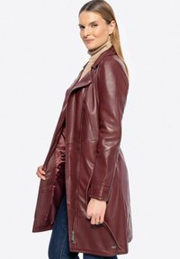 Giacca da motociclista in pelle bordeaux con design aderente, zip asimmetrica e tasche laterali. Texture liscia e finitura lucida.