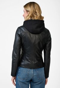 Svart läderjacka med svart huva, figursydd design, ribbade detaljer på ärmarna och slät yta, ihop med blå jeans.