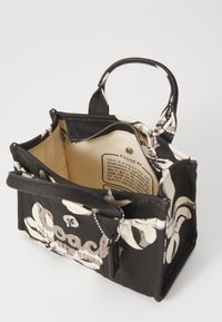 Borsa in tessuto nera con motivo floreale bianco, doppi manici, fodera interna, dettagli in metallo e etichetta del marchio visibile all'interno. Design compatto.
