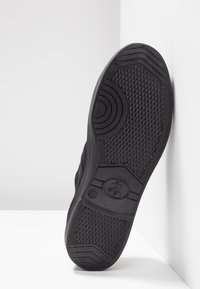 Suola di scarpa nera con gomma testurizzata per adesione, decorata con motivi circolari e esagonali, contrassegnata con un'etichetta di dimensione e un logo di bicicletta.