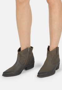 Botas de cuero marrón hasta el tobillo con punta afilada, cierre de cremallera, parte superior texturizada y tacón apilado; diseñadas para un ajuste elegante alrededor del tobillo.
