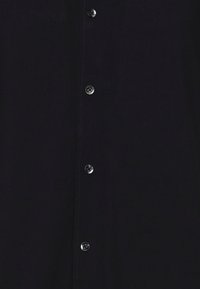 Chemise bleu marine foncé avec devant à boutons noirs, texture lisse et détails de couture subtils le long du plastron.