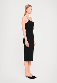 Black sleeveless dress with a fitted design, mid-calf length, and gold chain detail on the straps, made from a smooth material.