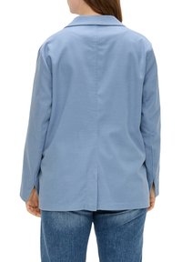 Chemise bleue à manches longues avec col, présentant une coupe droite et des fentes sur les côtés, fabriquée dans un tissu texturé. Vue de dos présentée.