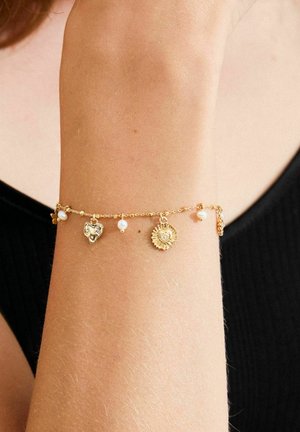 Pulsera de oro con varios dijes, incluyendo un corazón y un sol, intercalados con pequeñas perlas blancas en una cadena delicada.