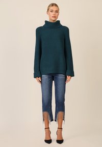 Maglione verde acqua a costine con colletto alto, abbinato a jeans blu strappati con dettagli in frange all'orlo e tacchi neri.