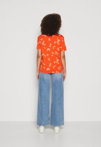 Rød T-shirt med blomsterprint og korte ærmer, parret med vidde letblå denim jeans og hvide platform sneakers. Bagview.