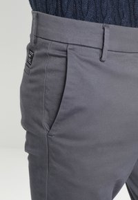 Gray cotton blend pants featuring a smooth texture, a slim silhouette, side pockets, and a fabric label on the waistband.