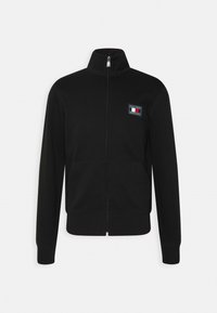 Felpa nera con zip realizzata in tessuto morbido, dotata di un colletto alto, due tasche frontali e una toppa con logo nella zona sinistra del petto.