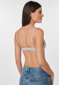Harmaa bralette, jossa on säädettävät olkaimet, sileä pinta ja hakasuljenta takana, yhdistettynä korkeavyötäröisiin kulutettuihin farkkushortseihin.