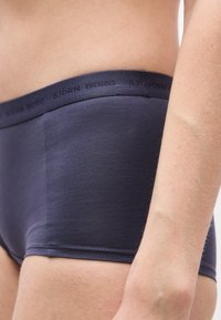 Κοντινό πλάνο ενός ατόμου που φοράει μποξεράκια Björn Borg σε ναυτικό μπλε, εμφανίζοντας τη ζώνη μέσης και μέρος του κορμού και του χεριού.