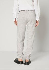 Pantalon de survêtement gris en tissu doux avec des poignets élastiques aux chevilles, associé à des baskets noires volumineuses. Poignets de chemise visibles.